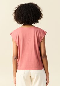 Lyhythihainen, korallinvärinen t-paita, jossa on rento istuvuus, pehmeä puuvillakangas ja huomaamaton ommeltu yksityiskohta kaula-aukossa, kuvattuna takaa.