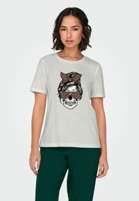T-shirt gris clair avec un graphique d'un crâne portant des lunettes de soleil et un nœud en imprimé léopard. Manches courtes et coupe décontractée.