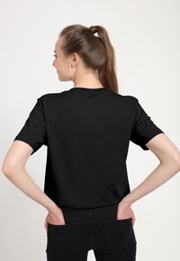 Svart kortärmad t-shirt tillverkad av bomull, med en klassisk rund halsringning och avslappnad passform, med en slät struktur och enkel baksidedesign.