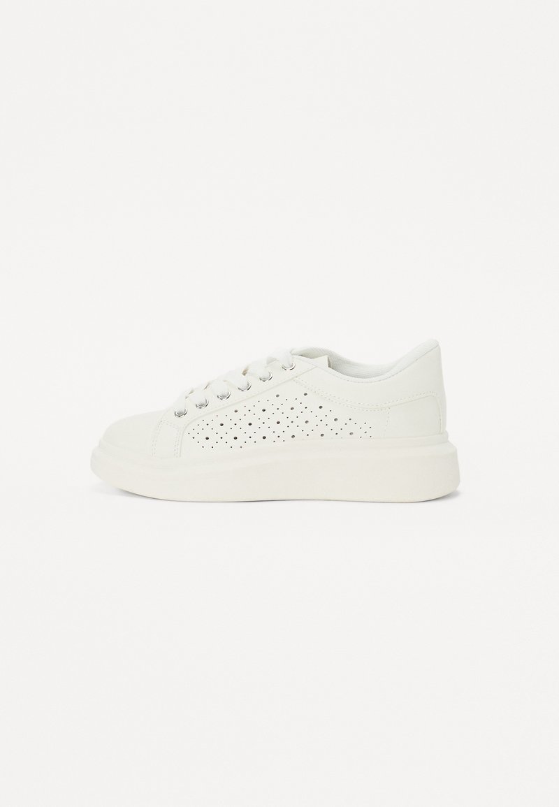 White sneaker with perforated pattern, smooth leather upper, round toe, flat rubber sole, and six metal eyelets for laces.