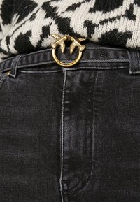 Svarta jeans i denim med en guldfärgad fågelformad bälte-spänne och en svartvitsrandig stickad tröja nedstoppad.
