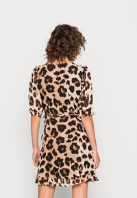 Robe imprimée léopard en tissu brun clair, avec des manches volantes, une taille cintrée et un ourlet évasé. Détails comprennent une taille à nouer et une texture douce.