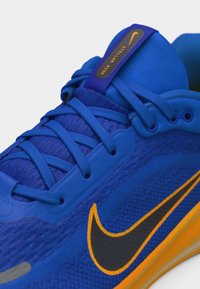 Chaussure de course Nike bleue avec un swoosh noir accentué de jaune, des lacets bleus et une étiquette "Stellar Ride" sur la languette.