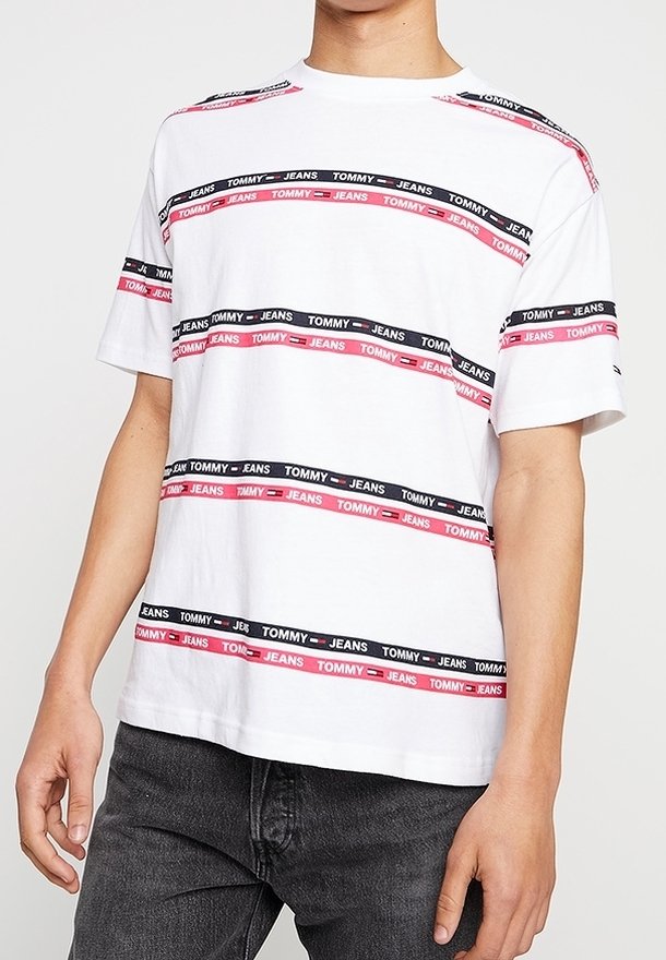 Vit bomulls t-shirt med röda och svarta horisontella ränder, försedd med upprepad text "TOMMY JEANS" och rundad halsringning.