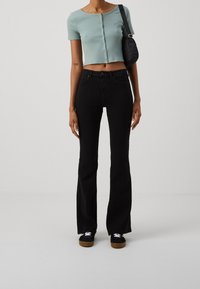 Haut court bleu clair à manches courtes avec fermeture boutonnée sur le devant, associé à un jean évasé noir et des baskets noires. Petit sac à bandoulière noir.