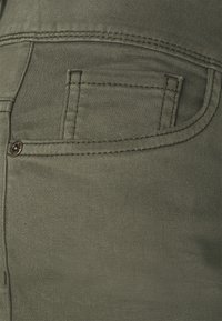 Olivově zelené bavlněné kalhoty s zadní nášivnou kapsou se zdobným švem a malým kovovým knoflíkem. Hladká textura a přiléhavý střih.