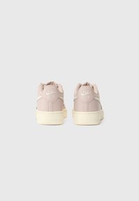 Nike Air joggesko i myk rosa skinn med en kremfarget gummisåle, med teksturerte detaljer og preget logo på hælen.