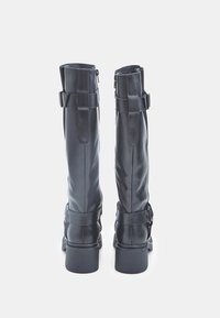 Botas de cuero negras hasta la rodilla con un acabado mate, que cuentan con un cierre de cremallera en la parte trasera y correas decorativas con hebillas. Tacones cuadrados y resistentes.