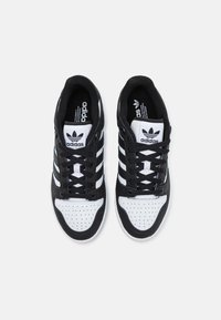 Čierno-biele tenisky Adidas s koženým zvrškom, perforovanou špičkou a dizajnom s tromi pruhmi. Šnúrky sú čierne s bielymi akcentmi.