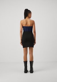 Black mini dress with a strapless blue denim bodice, fitted silhouette, and a back zipper. Worn with black knee-high boots.