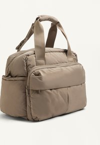 Beige gevoerde draagtas met dubbele handgrepen, een voorzak met rits en zijvakken, ontworpen voor reizen of dagelijks gebruik.