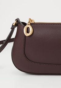 Burgunderfarbene Lederhandtasche mit goldenem Reißverschluss und Beschlägen. Verfügt über eine abgerundete Form und dezente Steppnähte. Abnehmbarer Schultergurt ist enthalten.