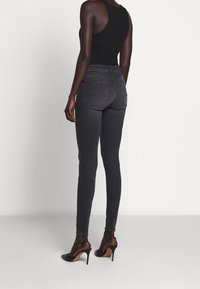 Top negro ajustado y jeans skiny gris oscuro vistos desde un ángulo trasero. Los jeans tienen bolsillos traseros y se combinan con zapatos de tacón negros.