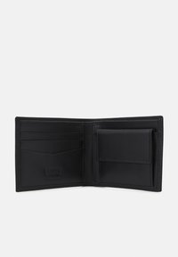 Portefeuille en cuir noir avec plusieurs emplacements pour cartes, une pochette photo et des coutures visibles. L'intérieur présente une texture lisse et un logo embossé.