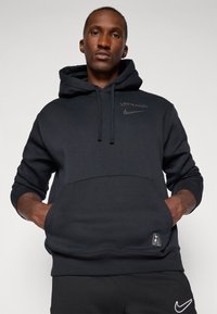 Dark grey Nike hoodie with a front pocket, drawstring hood, and logo accents. Soft fabric with ribbed cuffs and hem.