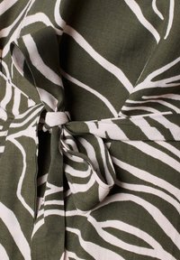 Tessuto a fantasia verde e bianco con strisce di zebra, con un dettaglio a fiocco legato in vita. Il materiale sembra avere una texture e un aspetto intrecciato.