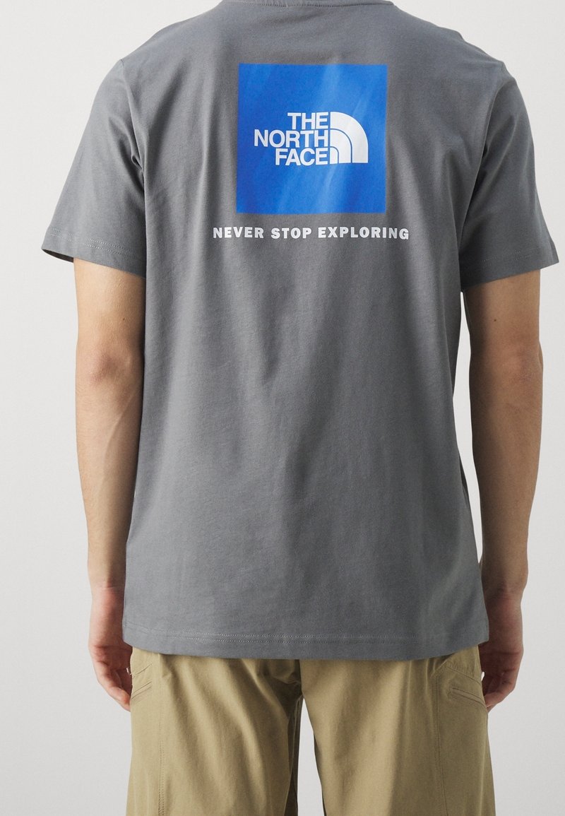 Harmaa puuvillapaita, jossa on sininen neliögraafikko, jossa lukee "THE NORTH FACE" -logo ja "NEVER STOP EXPLORING" -teksti valkoisella. Klassinen malli.