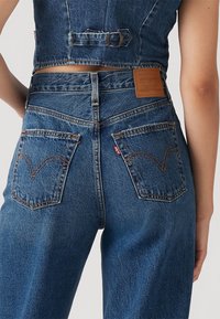 Denim-dress med tettsittende stroppeløs design, mørkeblå farge, kontrasterende sømmer, klassisk Levi's logoetikett og baklommer med buede sømmer.