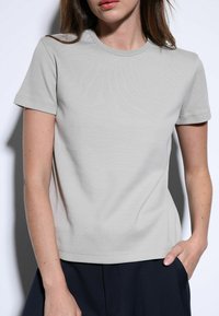 Lichtgrijs T-shirt met korte mouwen van zacht katoen, met een ronde hals en een effen textuur, gecombineerd met een donkere broek.