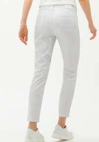 Pantalones slim-fit de color gris claro con un sutil patrón de rayas, cinco bolsillos y una cintura de altura media. Textura suave, combinados con zapatos blancos.