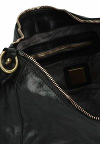 Zwarte leren tasinterieur met een gouden rits, voorzien van een ritsvak en een textiele voering. Een ronde hardware-ring is zichtbaar.