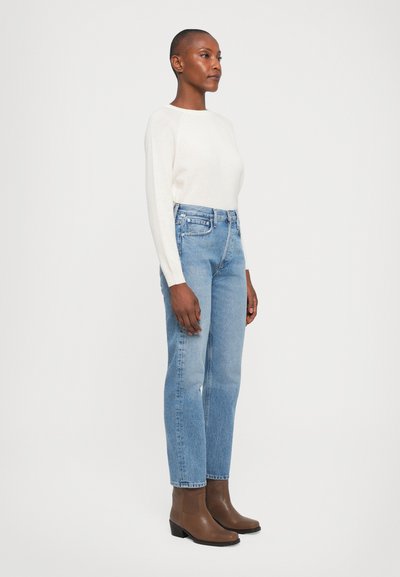 Light beige sweater, high-waisted light blue jeans, and brown ankle boots with a low heel. Straight-leg design and classic stitching details.