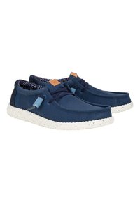 Chaussures en toile navy avec une semelle blanche mouchetée, un design à lacets et un accent en cuir tan sur la languette. Doublure intérieure rayée visible.