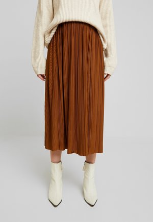 Jupe plissée marron avec un design fluide, associée à un pull crème et des bottines blanches. Le tissu présente une finition texturée.