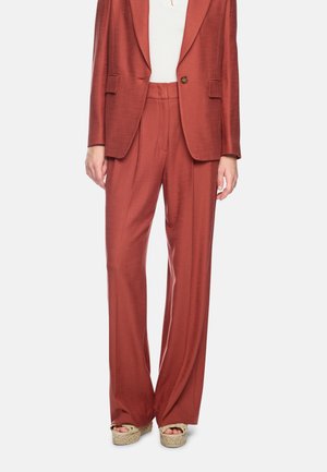 Woman wearing high-waist rust-colored wide-leg trousers with matching blazer and beige woven platform sandals on white background.