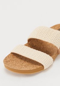 Světle béžové sandály s dvěma tkanými pásky a korkovou stélkou. Podešev je plochá a má hladký povrch. Jednoduchý a funkční design.