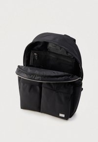 Svart ryggsekk laget av slitesterkt materiale, med et stort hovedrom, glidelås- lommer og to lommer foran for oppbevaring.