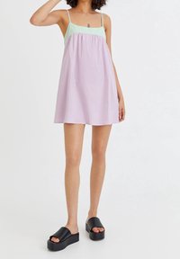 Robe à bretelles avec un haut vert menthe et des rayures verticales roses et blanches. Associée à des sandales à plateforme noires. Texture lisse.