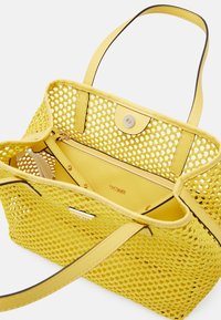 Sac fourre-tout tissé jaune présentant un design en mesh, des accents en cuir, une fermeture à pression et une poche intérieure zippée pour l'organisation.
