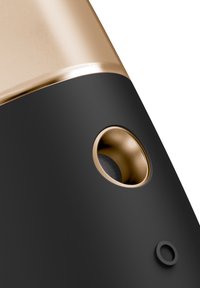 Svart och guld ljudanordning i närbild som visar en elegant design, rundade former, en texturerad grill över en rund högtalare och en texturerad knapp.