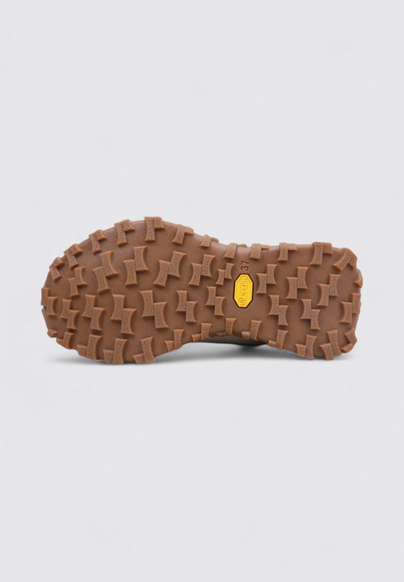 Vibram-sula med djupa, vinklade mönster i brunt. Har en central gul logotyp och upphöjda mönster för bättre grepp och dragkraft.