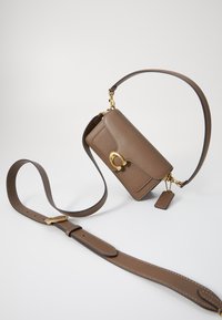Braune Leder-Crossbody-Tasche mit strukturiertem Finish, einem goldfarbenen Verschluss und einem verstellbaren Tragegurt mit rechteckigem Tag.