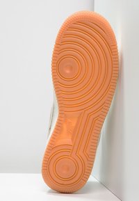 Sula av en Nike-sneaker med mönster av orange cirklar som vilar mot vita väggar och golv.