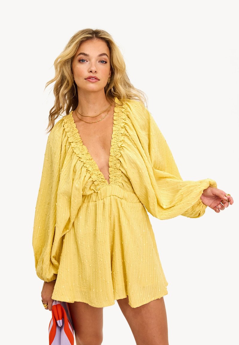 Robe jaune avec encolure froncée et longues manches bouffantes. Fabriquée dans un tissu texturé avec de subtils pois en relief. Coupe lâche, longueur au-dessus du genou.