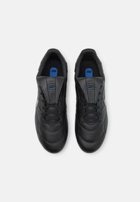 Zapatillas deportivas negras con un upper de cuero suave, acentos texturizados y un logo azul en la plantilla. Presentan cierre con cordones y un collar acolchado.