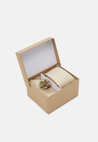 Corbata en tono dorado y pañuelo a juego en una caja de regalo de cartón marrón con interior blanco. Presenta un patrón texturizado y a rayas.