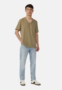 Olijfgroene T-shirt met korte mouwen en V-hals, gemaakt van lichtgewicht stof, gecombineerd met lichtblauwe jeans en witte sneakers met donkere accenten.