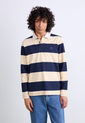 Langermet rugby skjorte i beige og marineblå striper, med krage, tre knapper foran, og et brodert logo på brystet.