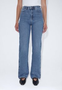 Džíny s vysokým pasem, rozšiřující se směrem dolů, v modré barvě s středním praním z denimu s kontrastním šitím. Mají zapínání na předním knoflíku a dvě boční kapsy.