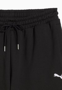Joggers de sport noirs avec une taille élastique, un cordon de serrage ajustable et un logo Puma blanc sur la cuisse gauche. Matière en coton doux.