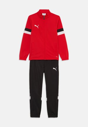 Rode trainingsjack met zwarte en witte strepen, rits sluiting en zijzakken, gecombineerd met zwarte broeken met witte accenten en logo.