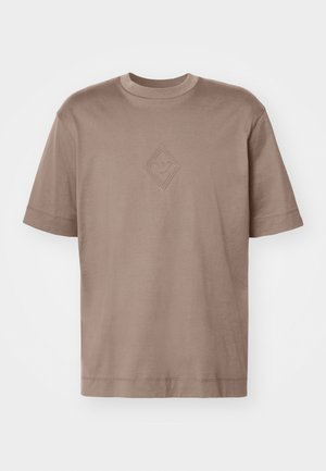 Korte ermer, lysebrun t-skjorte laget av myk bomull, med et preget diamantsymbol sentrert på brystet. Klassisk rund hals design.