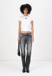 White cropped t-shirt with a round neck and logo detail, paired with gray straight-leg jeans and black ankle boots, holding a black handbag.