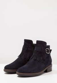 Svarta mocka ankelstövlar med rund tå, sidodragkedja, fransdetaljer och en dekorativ silverspänne på remmen. Låg klämd klack.