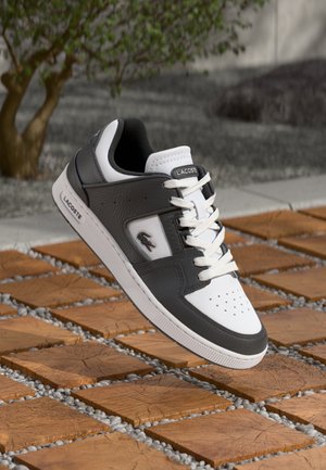 Black and white Lacoste sneakers with a textured leather upper, white laces, and perforated toe. Features logo detail and a cushioned collar.