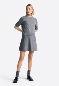 Grijs gebreid twee-delig outfit met een short-sleeved top en een uitlopende rok, beide versierd met kleine witte bloemapplicaties.